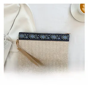 Detail of ethnic straw clutch bag with floral embroidery and brown leather wrist strap