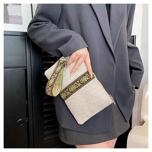 Detailed view of bohemian floral embroidery on a cream woven straw clutch with a zipper