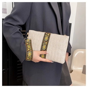 Close-up of beige woven clutch with ethnic floral embroidery and golden metal hardware