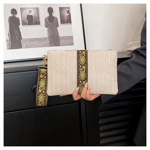 Detail of woven straw clutch featuring ethnic floral embroidery and golden zipper hardware