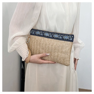 Close-up of straw woven clutch bag with blue floral embroidery and wrist strap detail