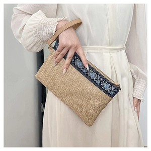 Detail showing straw woven texture, ethnic embroidery pattern, and leather wristlet strap