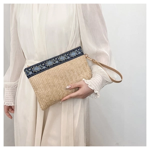 Detail of hand-woven straw clutch with ethnic floral embroidery and leather wrist strap