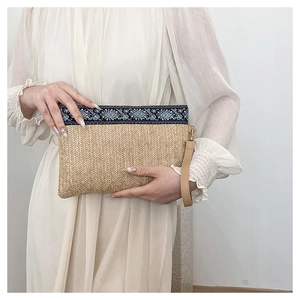 Detail of straw woven clutch featuring ethnic floral print trim and a leather wrist strap