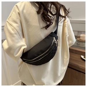 Detail of black quilted waist bag with gold zippers worn as a crossbody chest pack