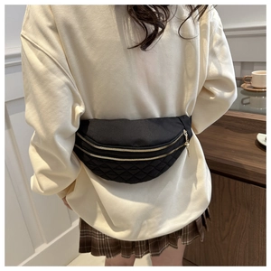 Detail of black quilted waist bag featuring dual gold zippers and diamond stitch pattern
