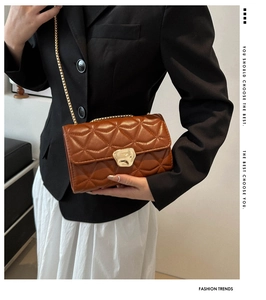 Detail of a brown quilted crossbody bag with a gold metal clasp and chain strap