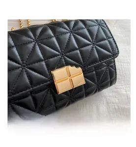 Primer plano del bolso acolchado negro con cierre cuadrado dorado y detalle de cadena