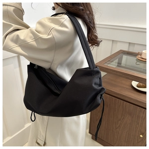Close-up of a black crescent shoulder bag with drawstring details and a wide strap