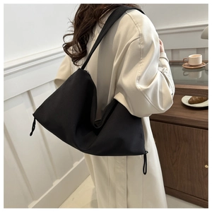 Side view of a large black canvas shoulder bag with drawstring detail on a model