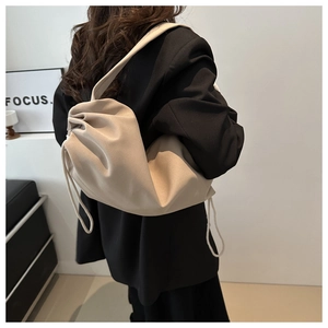 Detail of a beige drawstring cloud bag with a wide strap on a soft leather surface