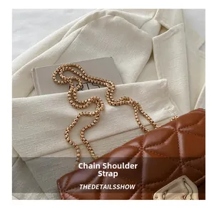 Detail of golden chain strap and metallic lock on caramel quilted shoulder bag