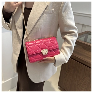 Close-up of fuchsia quilted chain bag with gold metallic buckle on a beige blazer