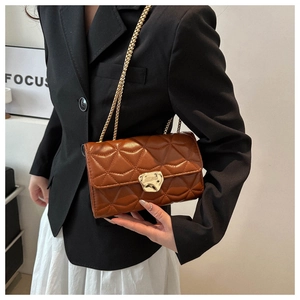 Brown quilted crossbody bag with gold chain strap shown on a black blazer and white skirt