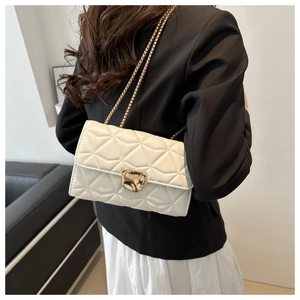 Close-up of white quilted chain bag with gold heart clasp worn over the shoulder