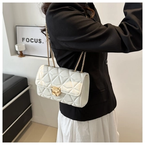 Detail shot of white quilted chain bag with gold tiger head lock on black blazer