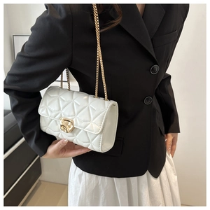 Detail shot of a white quilted crossbody bag with a gold chain strap and metal clasp