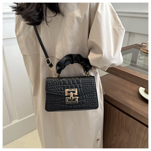 Detail showing the black crocodile pattern texture and golden geometric metal buckle of the bag
