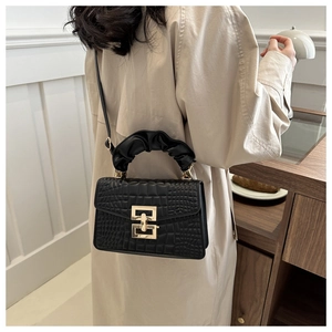 Detail of black crocodile texture bag with gold lock and ruched handle on a beige coat