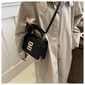 Detail of crocodile embossed leather bag with gold buckle and pleated handle on trench coat