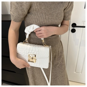 Close-up of white crocodile pattern handbag with gold clasp and pleated handle detail