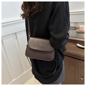 Détail d'un sac bandoulière carré marron foncé avec logo embossé sur du cuir mat