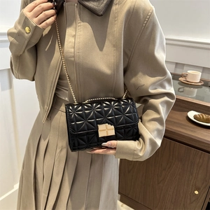 Bolso de hombro acolchado negro con cadena dorada usado por una modelo elegante