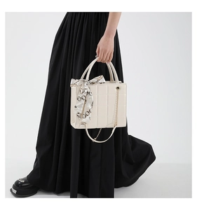 Detail einer gesteppten cremefarbenen Tasche mit Seidentuch und Goldkette