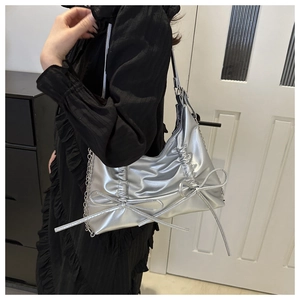 Close-up of metallic silver shoulder bag featuring bow details and pleated leather texture