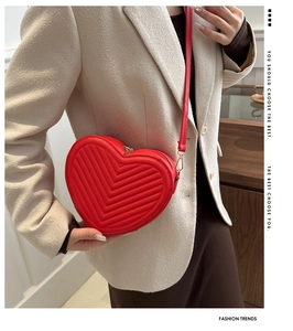 Detail of red heart-shaped quilted handbag with golden zipper on a beige suit outfit
