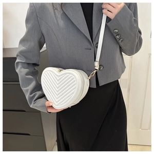 Close-up of heart-shaped white quilted crossbody bag worn with a gray blazer