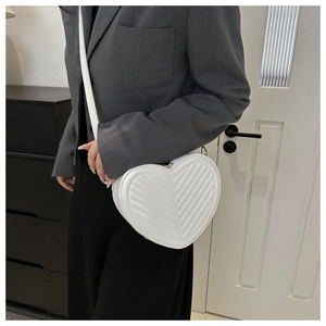 On-body view of a white heart-shaped crossbody bag with V-quilted stitching detail