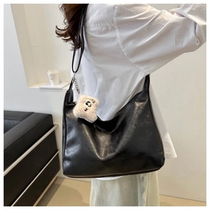 Close-up of black PU leather shoulder bag featuring a cream plush smiley face charm