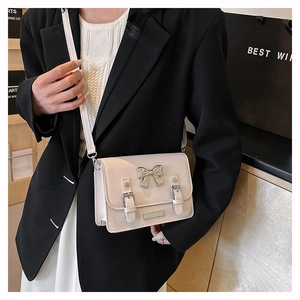 Detailed view of cream PU leather crossbody bag with silver bow buckle and adjustable strap