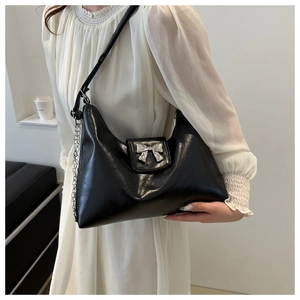 Detail of black faux leather tote bag featuring a silver metal bow and decorative chain