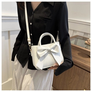 White bow-tie bucket bag detail showing matte PU leather and adjustable shoulder strap