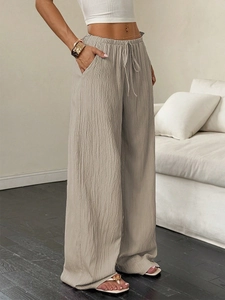 Detail of high-waist elastic drawstring and textured pleated fabric on wide-leg trousers