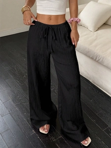 Detail of black wide-leg trousers featuring elastic drawstring waist and pleated fabric