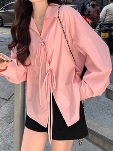 Détail d'une chemise rose à manches longues avec rubans à nouer et col rabattu élégant