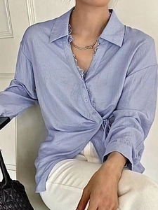 Detail of light blue wrap shirt featuring elegant lace trim and waist tie fastening