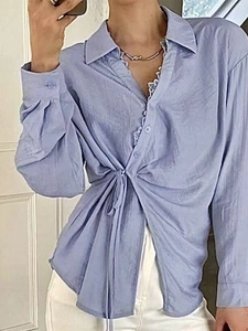 Detail of light blue long-sleeved shirt with waist tie and delicate white lace collar trim
