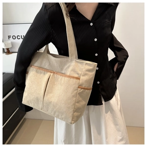 Detail of corduroy tote bag showing contrast brown leather trim and large front pockets
