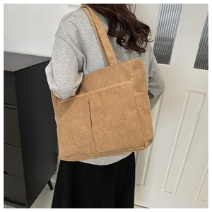 Brown corduroy tote bag with double front pockets shown on shoulder in a home setting