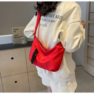 Side view of a red nylon half-moon crossbody bag with an adjustable black shoulder strap