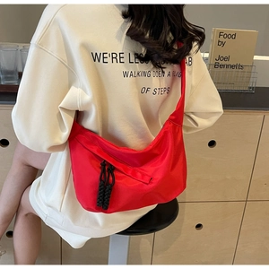 Detail view of a vibrant red crescent dumpling bag with black woven zipper on a model