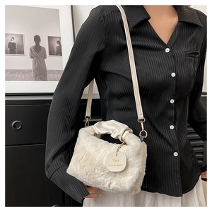 Detail of white faux fur shoulder bag with leather strap and decorative tag