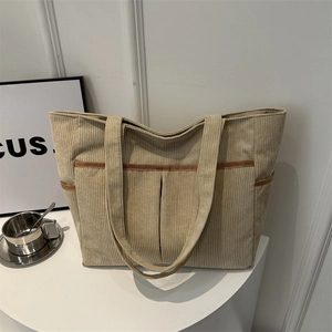 Beige corduroy large capacity tote bag with brown trim shown on a minimalist white table