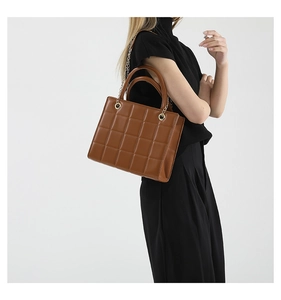 Brown quilted crossbody bag with gold chain strap shown on a model in high detail
