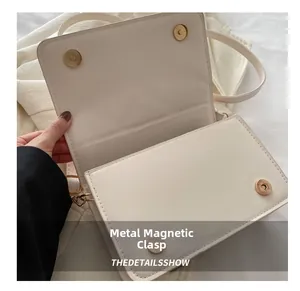 Détail des doubles boucles magnétiques dorées sur un petit sac carré beige texturé élégant