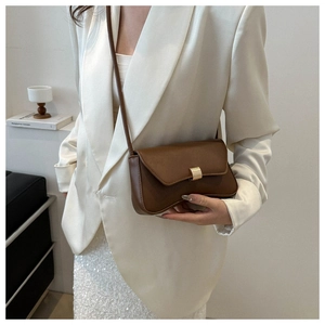 Chic brown leather shoulder bag with gold buckle styled on a white blazer outfit